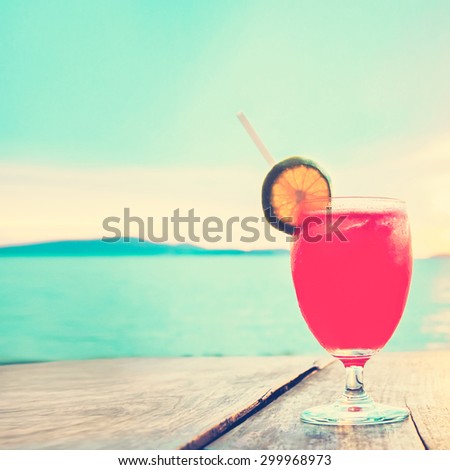 Unfocused cocktail drink on wood table in front of summer sea and sky background, vintage tone - chill out and summer holiday concept