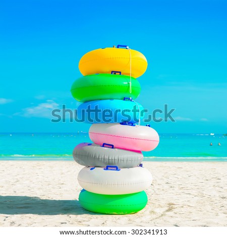 Stack of colorful rubber rings (or swim rings) on white sand beach - summer holiday concept