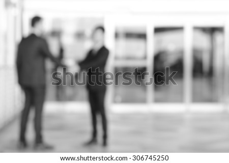Blurred image of businessmen making handshake in front of office building doors, monochrome effect