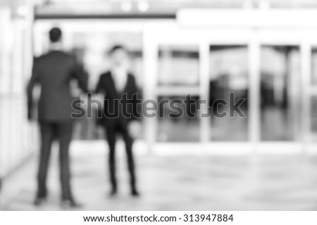 Blurred  image of businessmen making handshake in front of building glass doors, monochrome effect