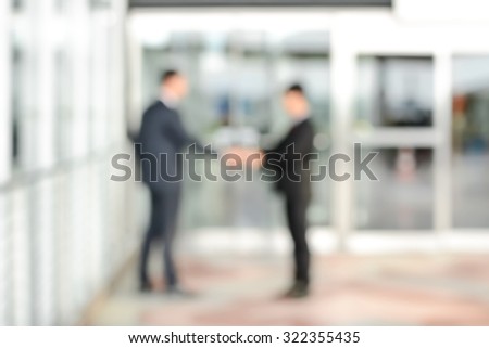 Blurred image of businessmen making handshake in front of office building doors, can be used as background