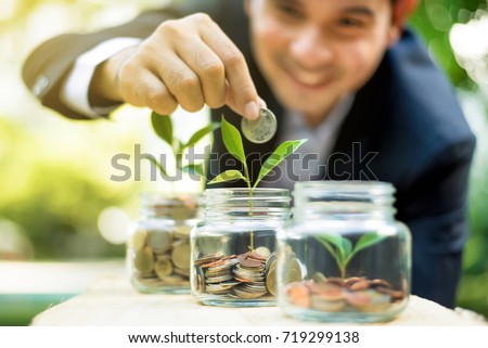 Businessman putting coin into the glass jar with young plant, demonstrating financial growth through saving plans and investment schemes Foto stock © 