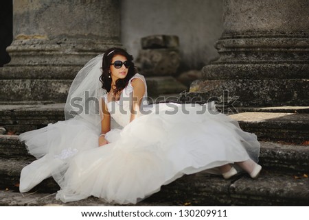 beautiful bride with sunglasses laying on the steps  of  an old church