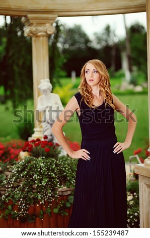 young woman  in blue dress posing in garden made in  Greek style