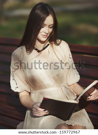 Red hair young woman sitting on bench reading book in autumn day.