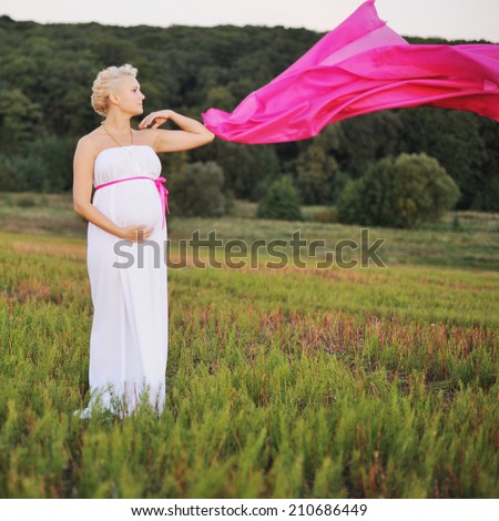 Young caucasian pregnant woman in a white greek dress with a pink bow at field.