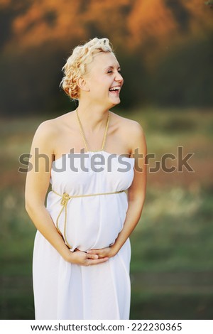 Portrait of  young pregnant woman in a white greek dress outside.