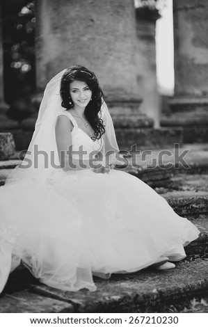Black and white picture of young bride wearing wedding dress and posing on steps of old church.