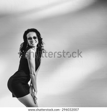 Black and white fashion portrait of young brunette woman wearing black dress, posing outdoor.