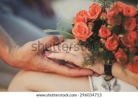 Jentle touch. Couple holding hands while woman has bouquet of roses.