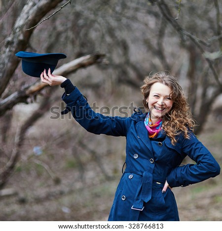 Here you go. Beautiful smile of curly hair young caucasian girl outdoors, wearing blue coat and hat, posing in autumn garden.