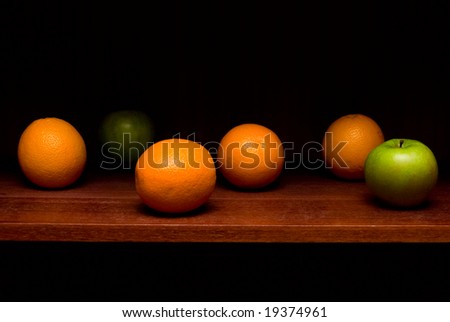 Some oranges and apples on the bookshelf