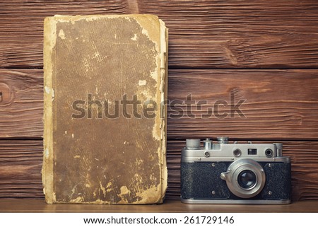 Retro 35mm film camera and old book over rustic wooden background