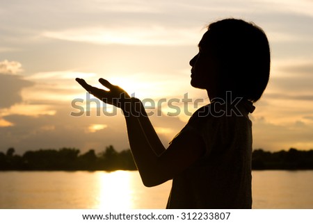 Silhouette of woman praying over beautiful sunset background.