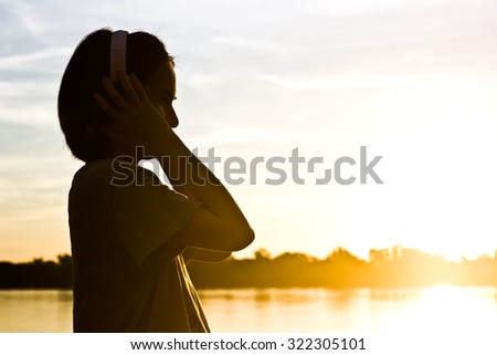 Silhouette of woman listening song over beautiful sunset background.