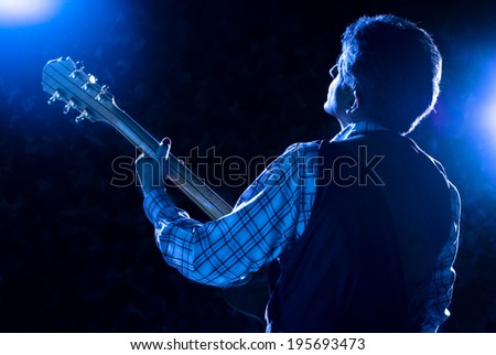 guitarist on stage playing guitar under blue light