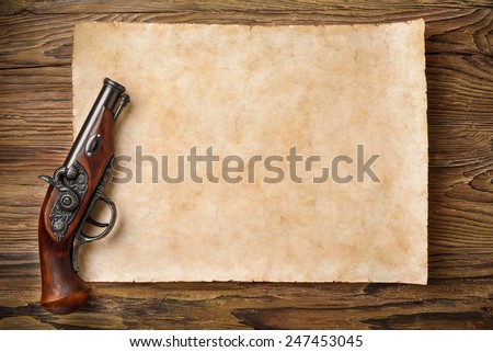old parchment with pirate pistol on aged wooden background