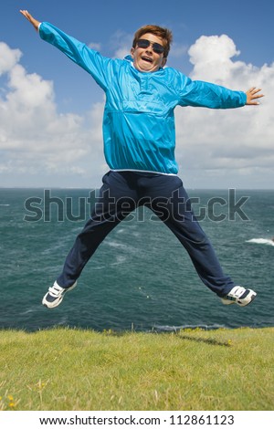 young boy jumping on the grass in front of the ocean during a beautiful sunny day
