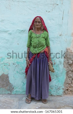 MANDAWA, INDIA - 17 OCTOBER 2013 - Full figure of unidentified old indian woman standing in front of a painted wall in the center of Mandawa, Rajasthan.