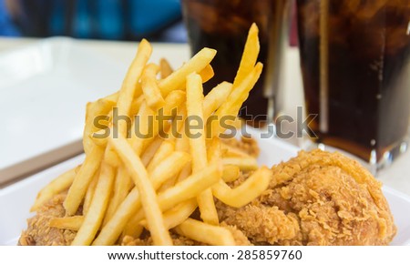 French fried with crispy fried chicken on white plate near two glasses of cola drink closeup