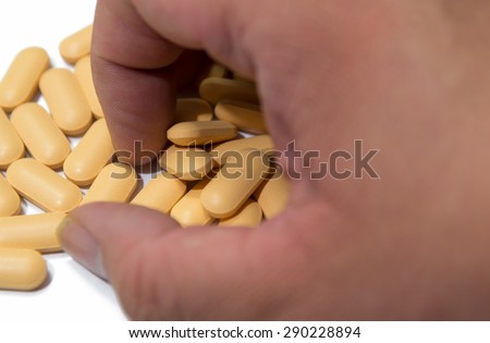 Male hand grabs yellow vitamin tablets focused on the piles of tablets isolated on white background