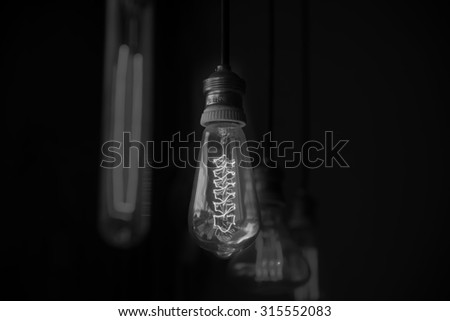 Hanged  decoration light bulbs focus on middle one  in dark room focused on the middle one vertical black and white