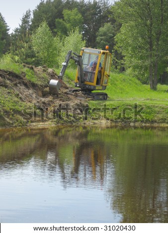 Earth mowing near the pond with small excavator