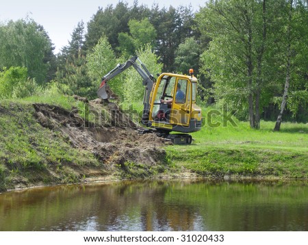 Earth mowing near the pond with small excavator