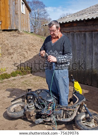 Senior country man outdoor, repairing old scooter