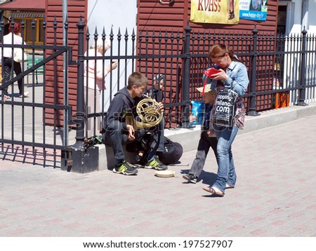 LIEPAJA,LATVIA - JUNE 8, 2014: Young street musician sits and plays the French horn to earn some money.