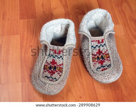 Warm knitted wool slippers with ornament on wooden floor close up.