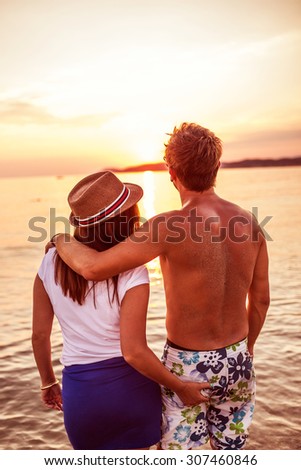 Summer couple at sunset on beach. Romantic young couple enjoying sun, sunshine, romance and love by the sea. Couple on summer vacation travel holiday.