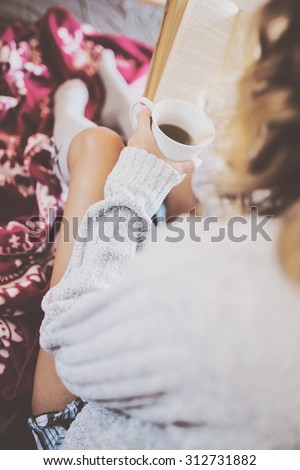 Soft photo of woman on the bed with cup of coffee reading book, top view point