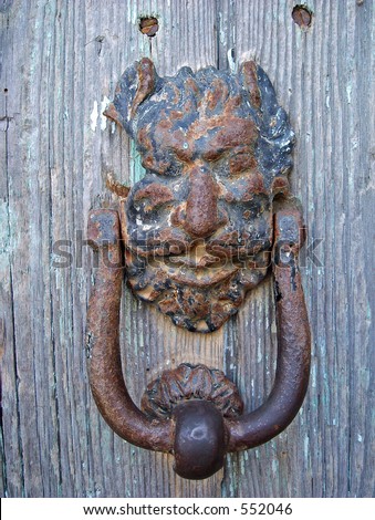 a rusty door knocker shaped as an ugly face on an old wooden door