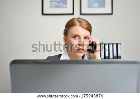 Red haired woman at the office, on the phone behind a laptop working.