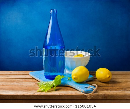 Still life with lemons and blue bottle on wooden table over grunge blue wall