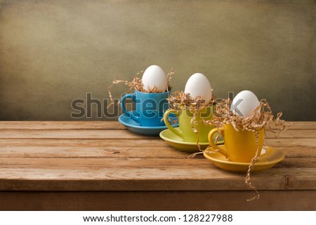 Background with easter eggs in coffee cups on wooden table