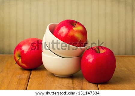 Red apple in stack of bowls on wooden table over vintage wallpaper