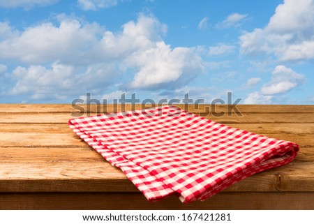 Red checked tablecloth and empty deck wooden table over blue sky