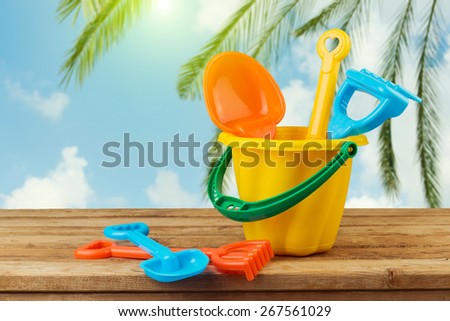 Children bucket and spade on wooden table over palm tree background
