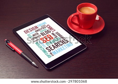 Digital tablet with SEO words and coffee cup on office desk