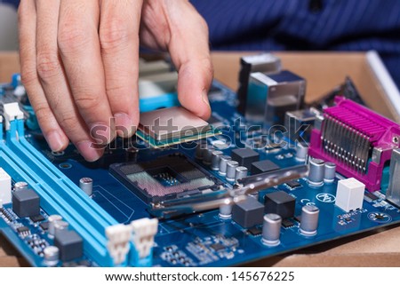Assembling high performance personal computer, inserting CPU, processor into the motherboard socket, opened PC case in background, shallow depth of field, focus on hand