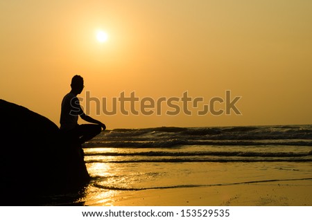 silhouette of young man sitting on the edge of rock at sunrise