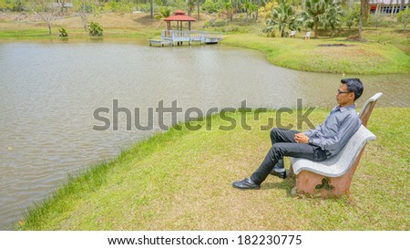 A young man sitting on the chair near the lake seeking for the peace