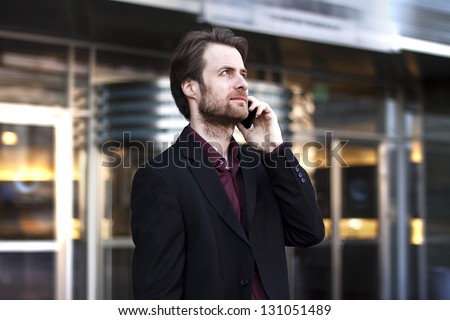 Forty years old businessman standing outside modern office building talking on a mobile phone