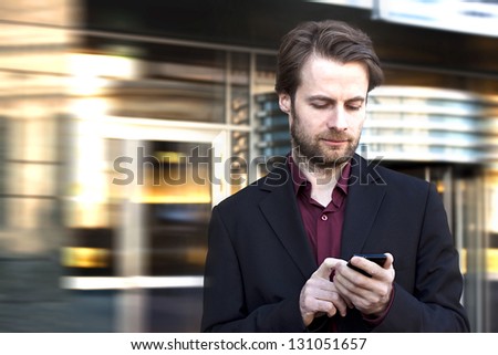 Forty years old businessman standing outside modern office building looking on a mobile phone