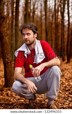 Forty years old runner man drinking water and having a rest after jogging workout in autumn forest