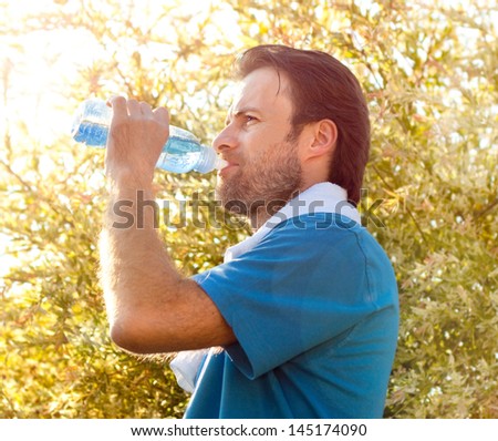 Forty years old caucasian active man drinking water and having a rest after workout during sunny summer day