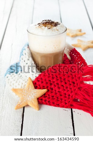 Winter latte coffee in a tall glass with star shaped christmas cookies and warm scarf on white planked wood background - rural still life
