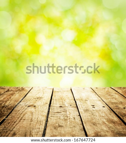 Spring rustic template background with text space. Old vintage planked wood table in perspective on fresh bright green bokeh - outdoor in the garden during sunny day.